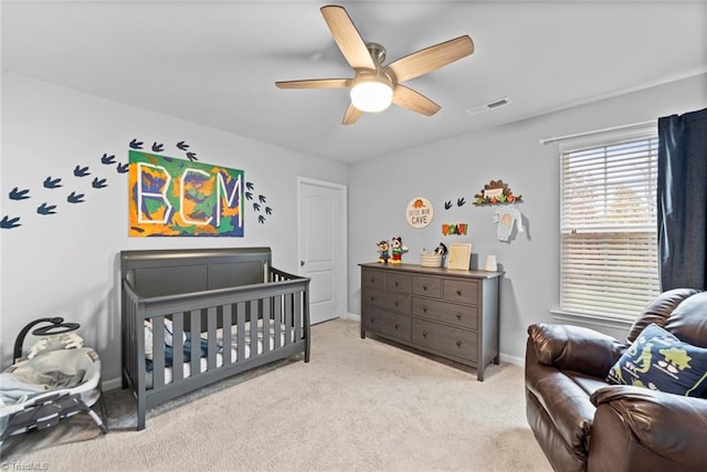 bedroom with ceiling fan, light colored carpet, and a crib