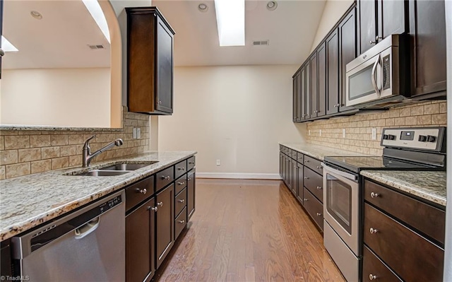 kitchen featuring stainless steel appliances, light stone counters, a sink, and dark brown cabinetry