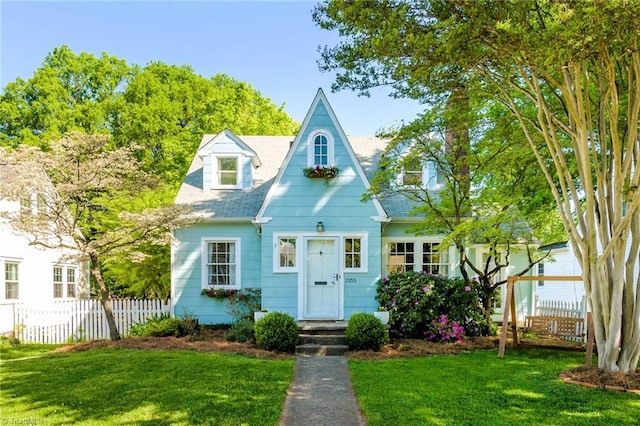 view of front of house featuring fence, roof with shingles, and a front lawn