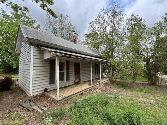 view of side of home with a chimney, metal roof, and covered porch