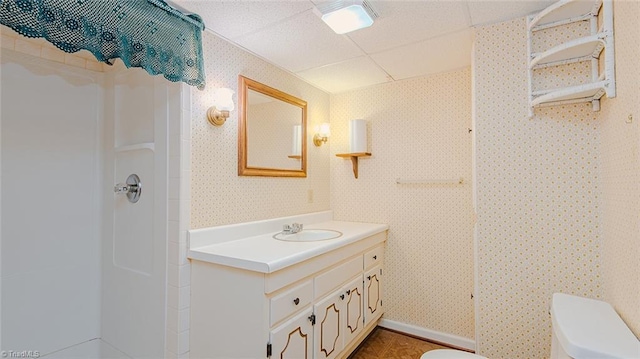 bathroom featuring toilet, vanity, a paneled ceiling, and a shower