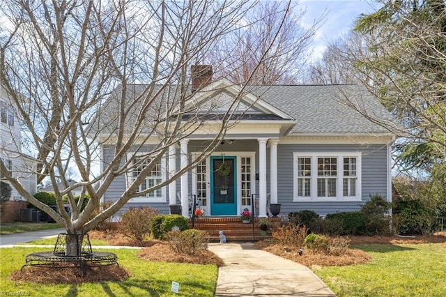 view of front of home featuring roof with shingles, a front lawn, a chimney, and a porch