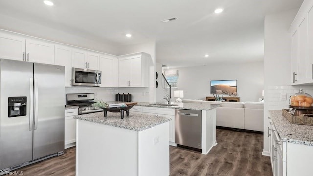 kitchen featuring open floor plan, white cabinetry, stainless steel appliances, a sink, and a peninsula