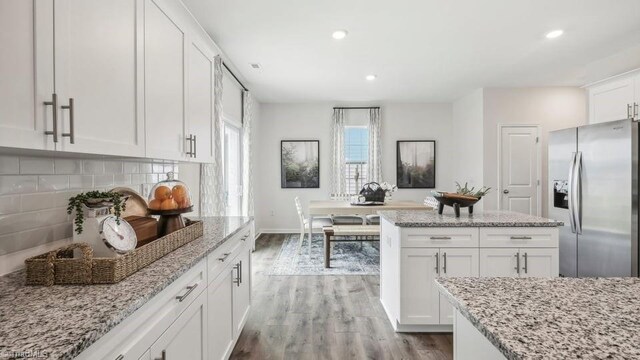 kitchen featuring white cabinets, wood finished floors, tasteful backsplash, stainless steel refrigerator with ice dispenser, and light stone counters