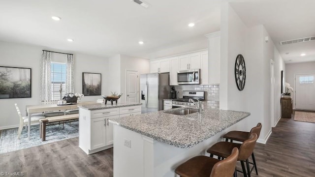 kitchen with visible vents, stainless steel appliances, dark wood finished floors, a sink, and a center island