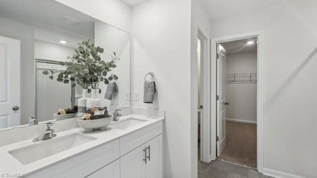 full bath with double vanity, a spacious closet, and a sink