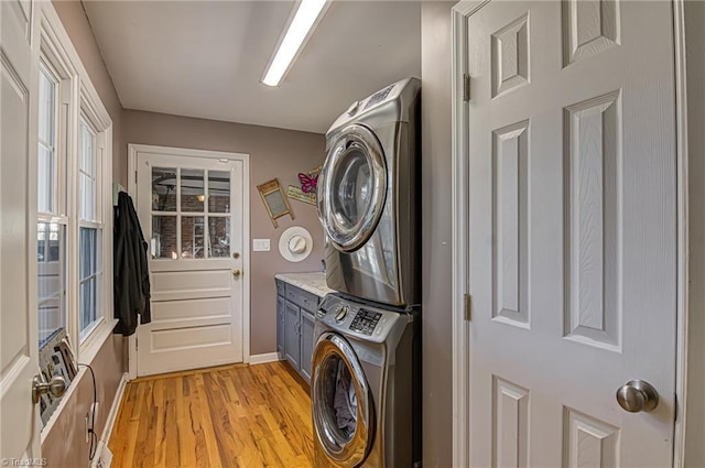 laundry room with cabinets, stacked washing maching and dryer, and light hardwood / wood-style floors