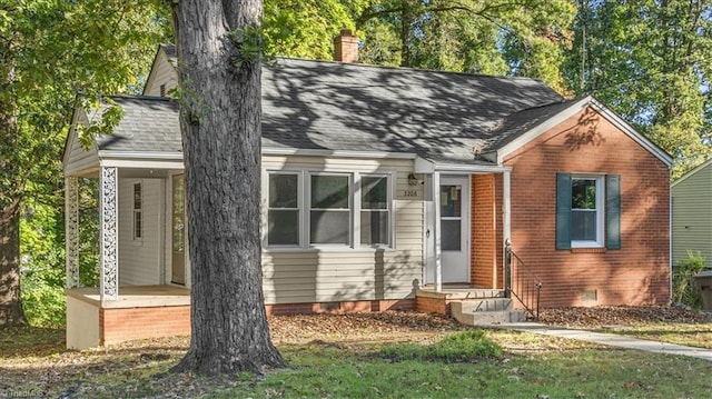 view of front of home with covered porch, a shingled roof, brick siding, crawl space, and a chimney