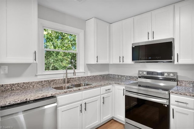 kitchen with light stone counters, appliances with stainless steel finishes, light wood-style floors, white cabinetry, and a sink