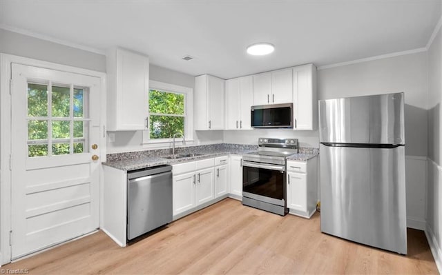 kitchen with stainless steel appliances, a sink, white cabinets, light stone countertops, and light wood finished floors