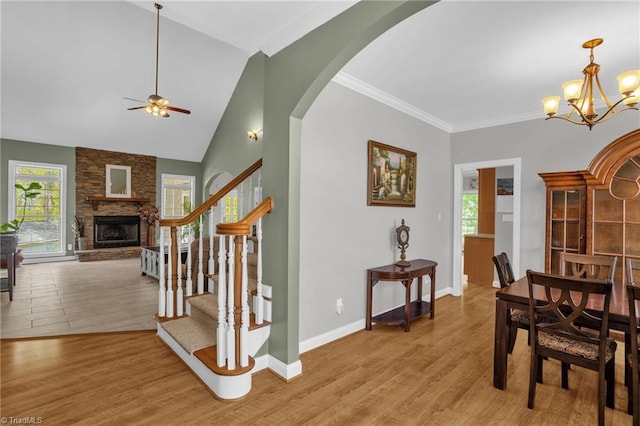 dining space with stairs, a stone fireplace, light wood-style flooring, arched walkways, and ceiling fan with notable chandelier