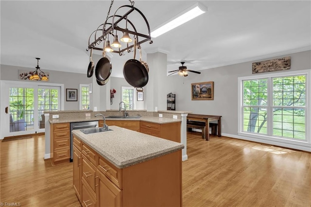 kitchen featuring light stone countertops, an island with sink, decorative light fixtures, light wood-style floors, and a sink