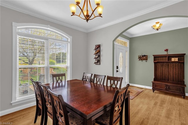 dining area with arched walkways, an inviting chandelier, light wood-style floors, ornamental molding, and baseboards