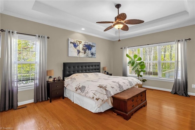 bedroom featuring multiple windows, a raised ceiling, and light wood-type flooring