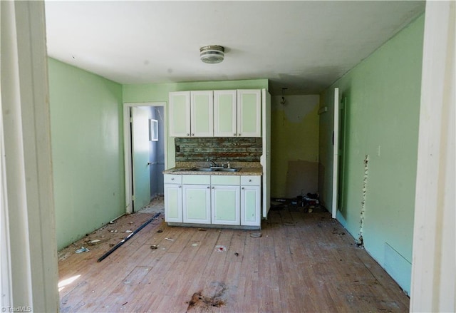 kitchen with a sink, light wood-type flooring, backsplash, and white cabinetry