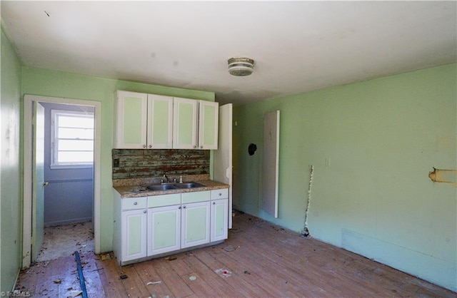 kitchen with a sink, light wood-type flooring, decorative backsplash, and white cabinetry