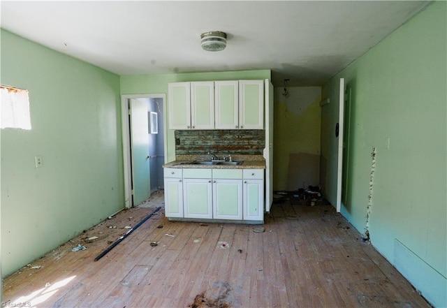 kitchen featuring a sink, tasteful backsplash, light wood-style flooring, and white cabinetry