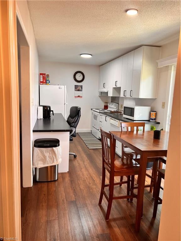 kitchen featuring a textured ceiling, dark wood-type flooring, white appliances, and white cabinetry