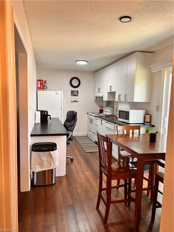 kitchen with white appliances, dark hardwood / wood-style flooring, white cabinetry, and a textured ceiling