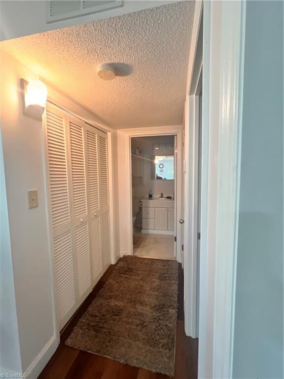 corridor with a textured ceiling and dark hardwood / wood-style flooring