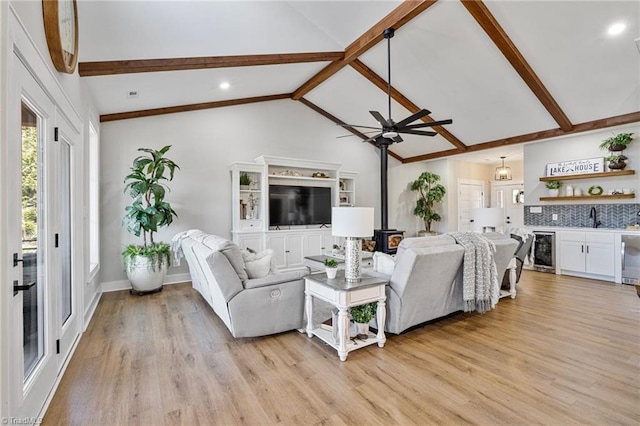 living room featuring a wood stove, indoor wet bar, vaulted ceiling with beams, wine cooler, and light wood-type flooring