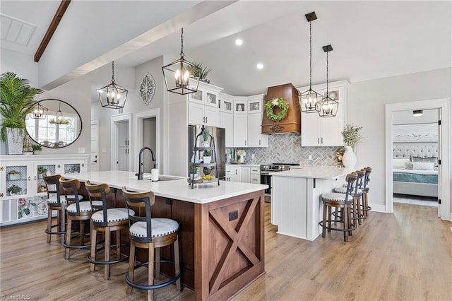 kitchen featuring sink, stainless steel appliances, custom range hood, an island with sink, and white cabinets