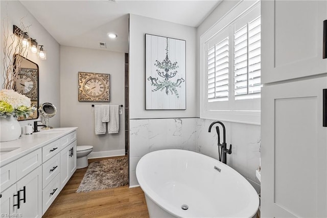 bathroom featuring wood-type flooring, tile walls, a tub to relax in, vanity, and toilet