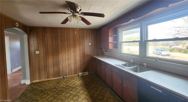 kitchen featuring ceiling fan, sink, black dishwasher, crown molding, and wooden walls