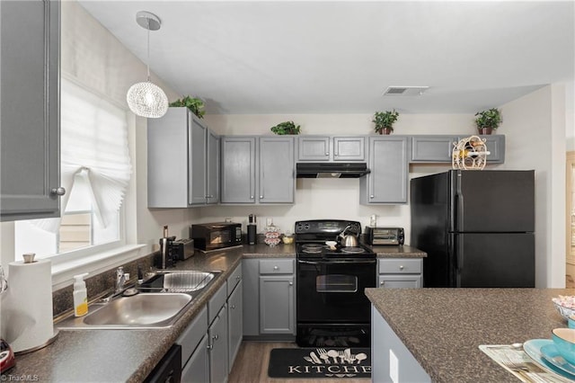 kitchen with gray cabinets, a sink, black appliances, under cabinet range hood, and dark countertops