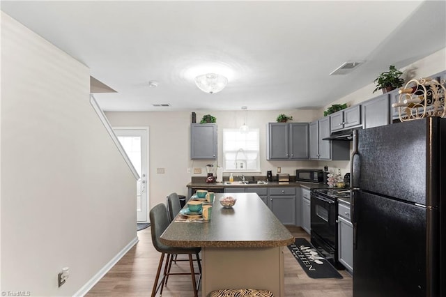 kitchen featuring visible vents, gray cabinets, black appliances, a kitchen bar, and dark countertops