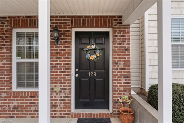 view of exterior entry with brick siding and covered porch