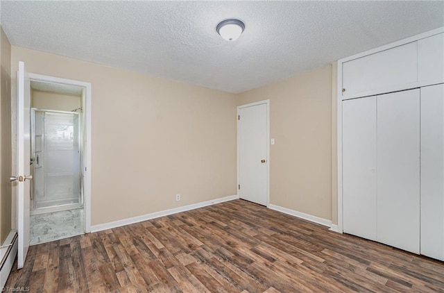 unfurnished bedroom featuring wood finished floors, a textured ceiling, baseboard heating, ensuite bath, and a closet
