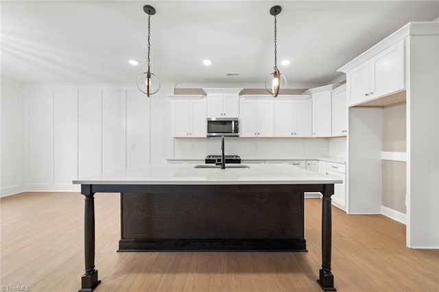 6957 Orchard Path Dr, Clemmons, NC 27012 - kitchen featuring stainless steel microwave, a sink, backsplash, light wood finished floors, and a kitchen island with sink