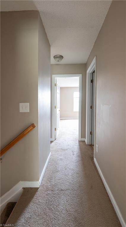 corridor with a textured ceiling and light carpet