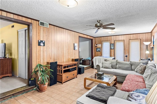 living area with wooden walls, ceiling fan, ornamental molding, a textured ceiling, and light tile patterned floors