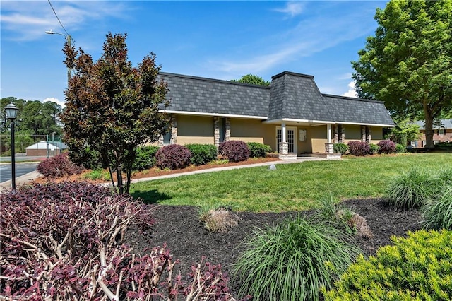 front of property with mansard roof, a front yard, roof with shingles, french doors, and stucco siding