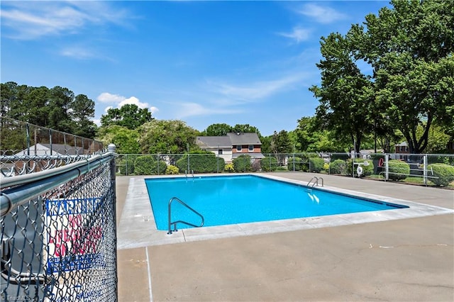 community pool with fence, a patio, and view of wooded area