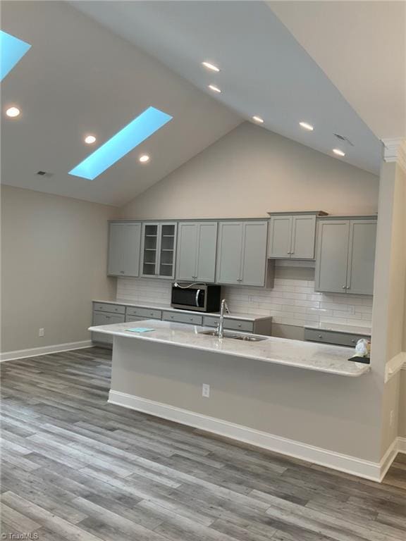 kitchen featuring dark wood finished floors, stainless steel microwave, gray cabinetry, glass insert cabinets, and a sink