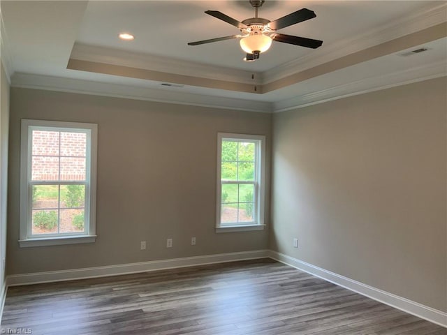 spare room with ornamental molding, a tray ceiling, wood finished floors, and baseboards