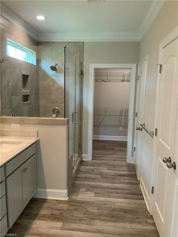 full bathroom featuring a spacious closet, ornamental molding, a stall shower, vanity, and wood finished floors