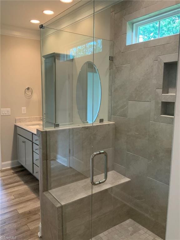 bathroom featuring baseboards, ornamental molding, wood finished floors, vanity, and a shower stall