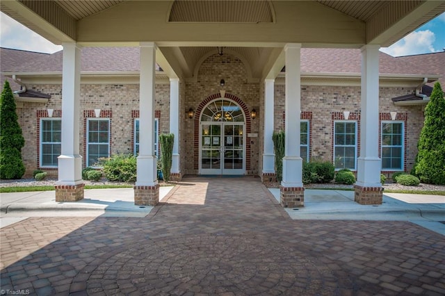 view of exterior entry featuring french doors, brick siding, and roof with shingles