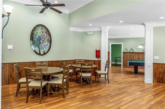 dining area featuring a wainscoted wall, crown molding, wood finished floors, and ornate columns