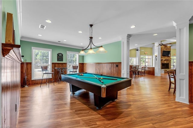 game room with a wainscoted wall, visible vents, a stone fireplace, wood finished floors, and ornate columns