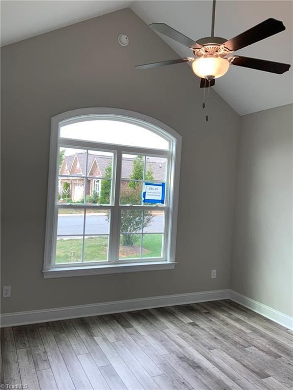 empty room featuring light wood-type flooring, vaulted ceiling, and baseboards