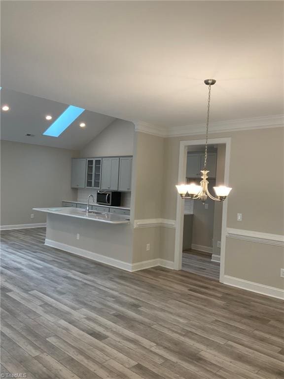 kitchen with a notable chandelier, stainless steel microwave, gray cabinetry, dark wood-type flooring, and a sink