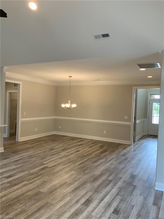 empty room featuring visible vents, a chandelier, wood finished floors, and ornamental molding