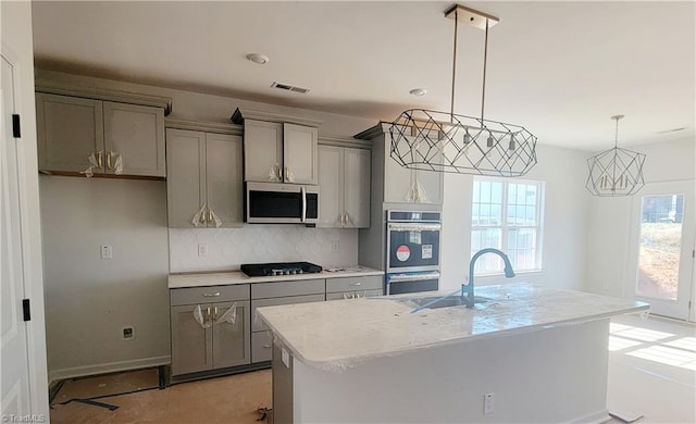 kitchen with a center island with sink, gray cabinetry, appliances with stainless steel finishes, and tasteful backsplash