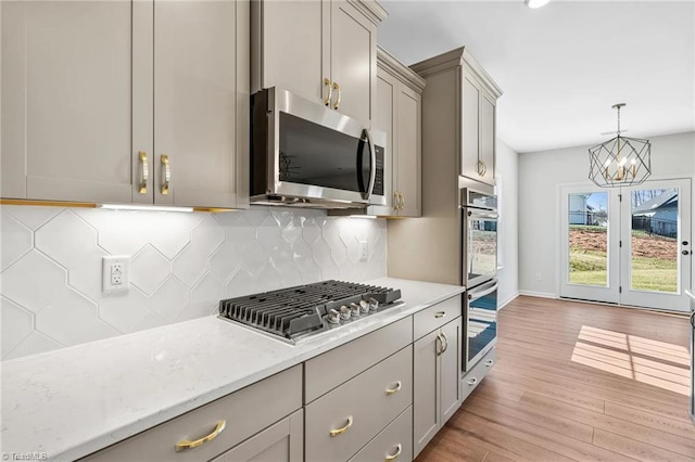 kitchen featuring decorative backsplash, stainless steel appliances, an inviting chandelier, light hardwood / wood-style flooring, and gray cabinets