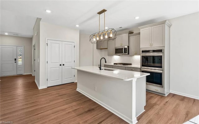 kitchen featuring sink, gray cabinets, light wood-type flooring, decorative light fixtures, and stainless steel appliances